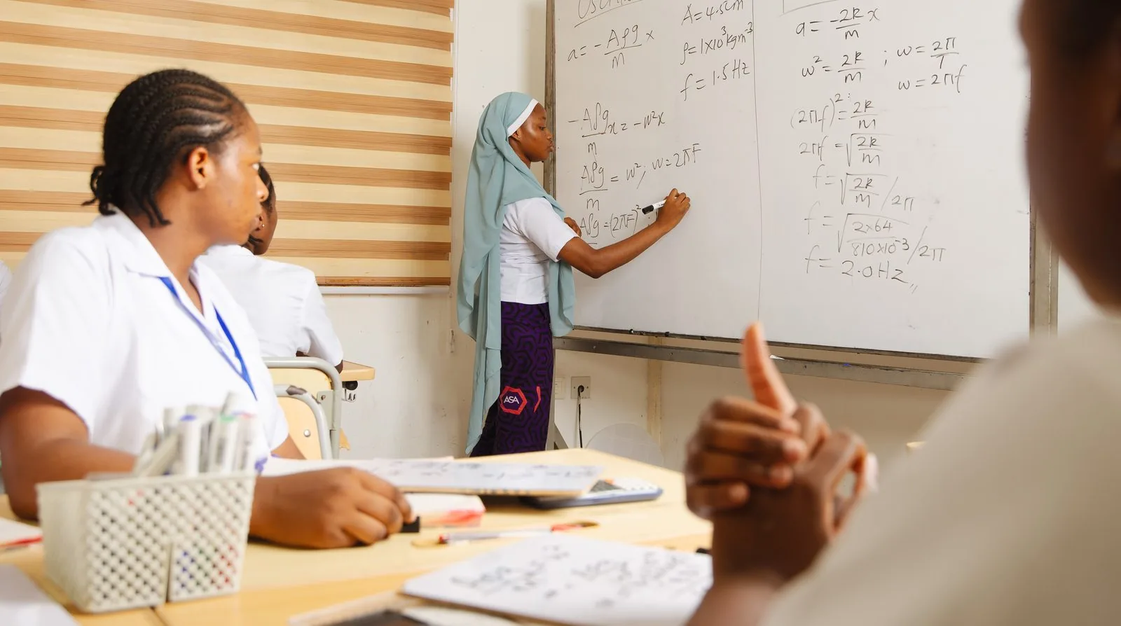 An ASA student working through physics equations at the whiteboard